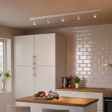 Cocina moderna con armarios blancos, encimera de madera, focos BÄVE y vista a la vegetación.