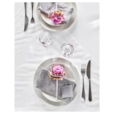 Elegante mesa con platos blancos, servilletas grises, decoración de flores rosas, vasos transparentes y cubiertos de plata BEHAGFULL.