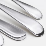 Cuatro cuchillos de acero inoxidable pulido dispuestos ordenadamente, reflejando la luz, sobre una superficie blanca.