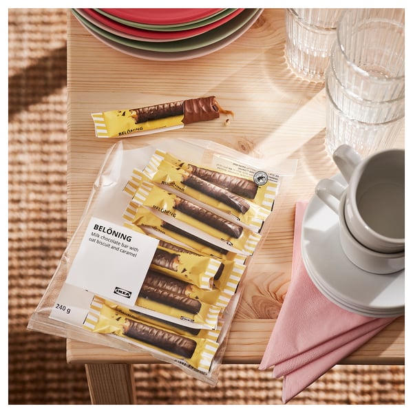Tabletas de chocolate IKEA BELÖNING, empaquetadas y parcialmente sin envolver, cerca de platos y tazas.
