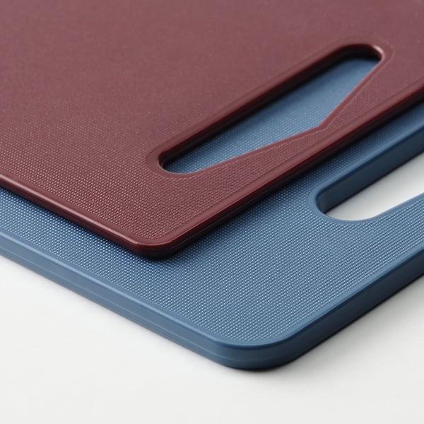 Dos tablas de cortar de colores apiladas, una granate, otra azul, con bases y asas antideslizantes.