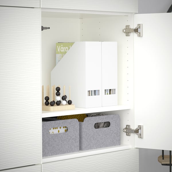 Mueble BESTÅ blanco con estantes que contienen cubos de fieltro gris y decoración. Las bisagras permiten ajustar la puerta.