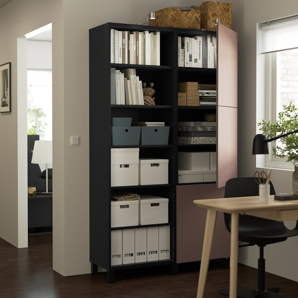 Mueble de almacenaje BESTÅ negro con estantes para libros y cajas de almacenamiento, junto a un escritorio en una oficina en casa.