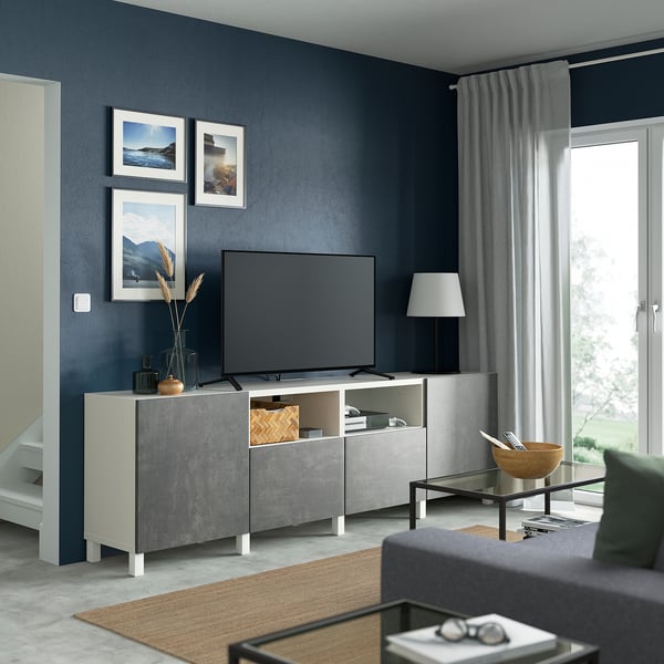 Banco de tv BESTÅ gris, estantes ajustados, cajón organizado, sofá verde, pared azul oscuro, cuadros enmarcados.