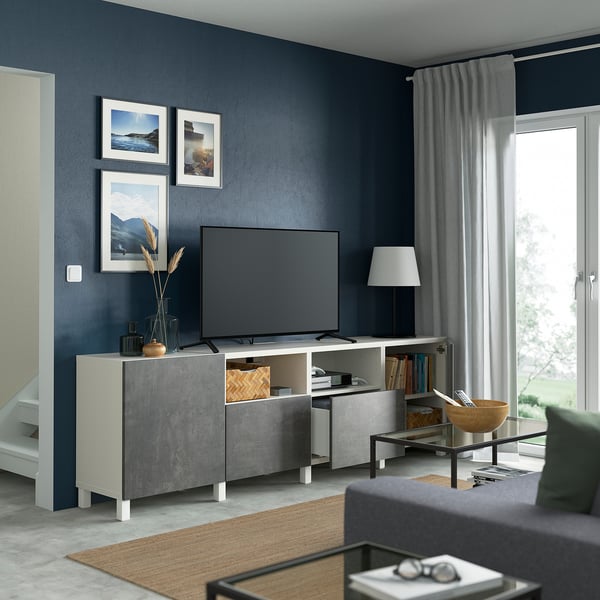 Sala de estar moderna con mueble de TV BESTÅ gris, TV de pantalla plana, cortinas grises, lámpara y elementos decorativos.