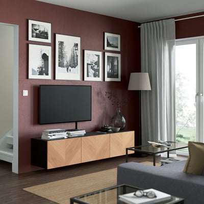 Sala de estar moderna con paredes de color burdeos, TV grande en la unidad BESTÅ, madera y negro.