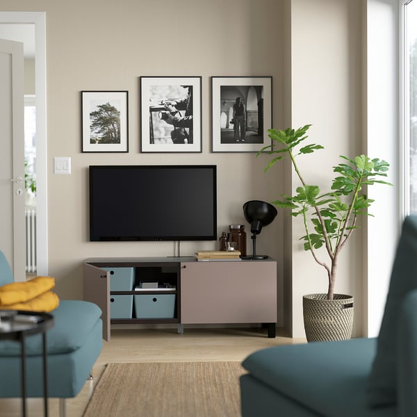 Sala de estar moderna con mueble de TV BESTÅ, libros, decoración. Arte en blanco y negro, almacenamiento azul, planta verde, sillas azules con almohada amarilla.