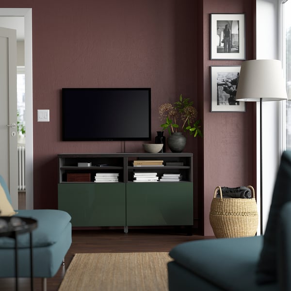 Sala de estar moderna con banco de televisión verde BESTÅ, libros y decoración. Pared de color púrpura oscuro, asientos azules y cesta de mimbre.