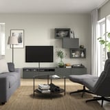 Moderna sala de estar con banco de televisión BESTÅ en gris, con TV de pantalla plana, muebles grises, suelo de madera, mesa de centro de cristal y decoración minimalista.