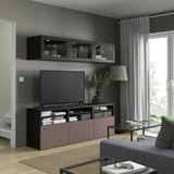 Sala de estar moderna con almacenamiento de TV BESTÅ, marco negro, cajones de rosetas, TV de pantalla plana, sofá gris, grandes ventanales.