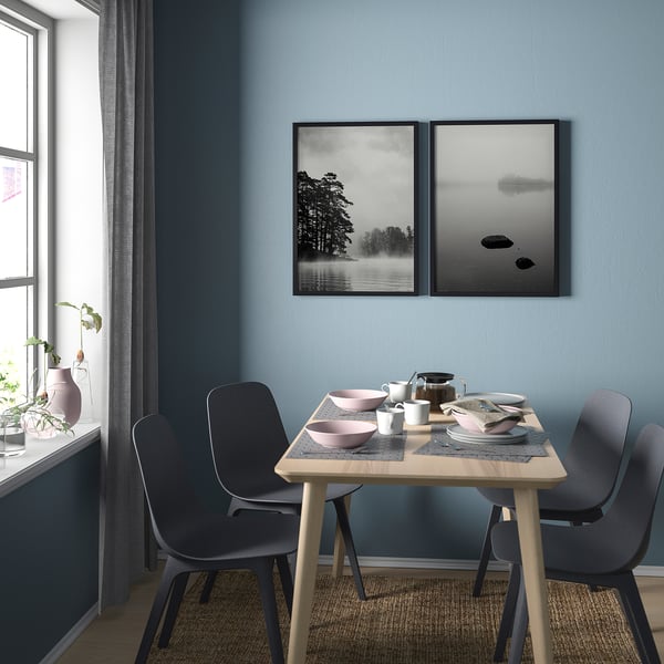 Comedor moderno con sillas azules, mesa de madera y dos impresiones artísticas de la naturaleza enmarcadas en blanco y negro en la pared azul.