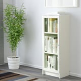 Librería BILLY con puertas de vidrio, libros y planta.