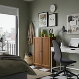 Acogedor dormitorio con librería Billy, escritorio, silla, sábanas verde oliva y pared verde con arte y reloj.