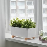 Jardinera blanca en soporte de madera junto a la ventana con planta verde. Mejora la decoración de la cocina y levanta las plantas para una mejor vista.