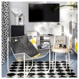 Sala de estar moderna con silla de lunares blancos y negros, cojines, alfombra y una mesa de vidrio con copas de champán.