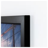 Obra de arte enmarcada en negro montada sobre una pared blanca. El marco es elegante y está bien ensamblado, lo que indica alta calidad.