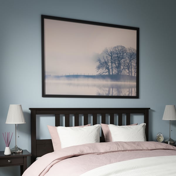 Gran arte paisajístico enmarcado sobre una cabecera de cama negra, creando un ambiente sereno en una habitación azul.