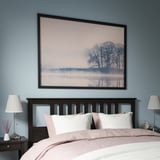 Gran arte paisajístico enmarcado sobre una cabecera de cama negra, creando un ambiente sereno en una habitación azul.