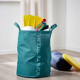 Bolsa de almacenamiento verde azulado con coordenadas oceánicas, que sostiene juguetes deportivos en suelo de madera clara.