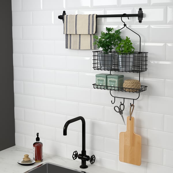 Cocina moderna con estante de almacenamiento montado en la pared con toallas para colgar, plantas y utensilios de cocina. Grifo negro y azulejos blancos del metro visibles.