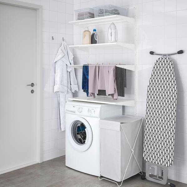 Área de lavandería blanca organizada con almacenamiento BOAXEL, lavadora, secadora y tabla de planchar.