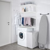 Área de lavandería blanca organizada con almacenamiento BOAXEL, lavadora, secadora y tabla de planchar.