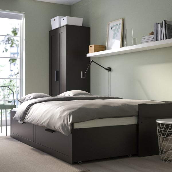 Dormitorio moderno con sofá cama BRIMNES gris, cajones de almacenamiento y estantes montados en la pared.