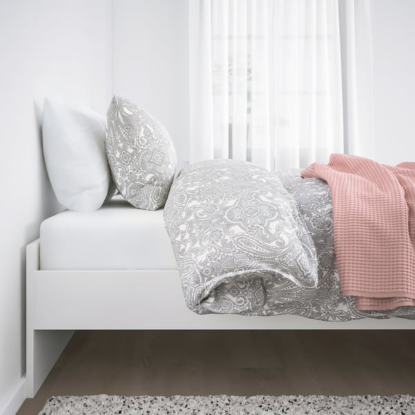 Cama de tonos neutros con ropa de cama con intrincados patrones y almohadas suaves, que muestran un diseño compacto.
