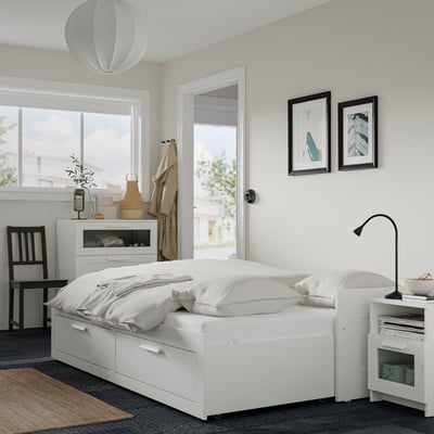 Dormitorio moderno con sofá cama BRIMNES blanco, cajones y muebles a juego. Bien iluminado con luz natural y decoración.