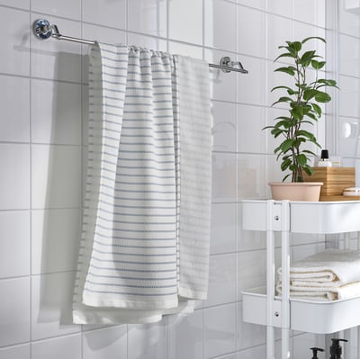 Baño moderno con toallero cromado BROFJÄRDEN , toallas blancas y una planta verde en una estantería blanca de tres niveles.