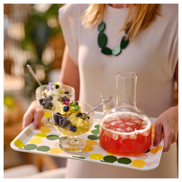 Persona sosteniendo la bandeja con puntos amarillos. La bandeja tiene postres de frutas y bebida con hielo. El borde en ángulo mantiene los artículos seguros.
