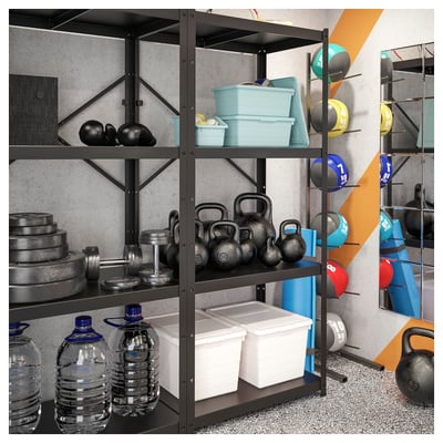 Sistema de estanterías BROR negro para gimnasio en casa que almacena botellas de agua, pesas rusas y recipientes de plástico. El equipo está perfectamente organizado contra la pared gris.