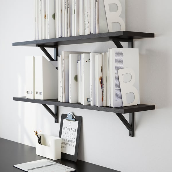 Estanterías de pared negras con libros y artículos de decoración. Incluye un portapapeles con lápices.