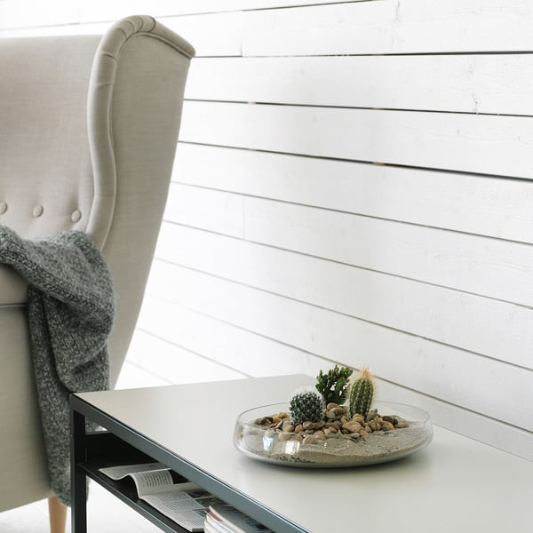 Sala de estar moderna con silla gris claro, pared de shiplap blanca, mesa blanca y cuenco de vidrio con cactus.