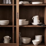 Estante de madera con gres blanco DAGGASTER; platos, cuencos, tazas; pilas ordenadas; beige claro, mate, moteado; tamaños variados.