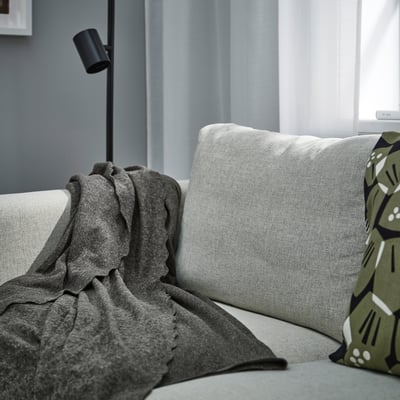 Manta de felpa gris DAGGKÅPOR en el sofá, suave y de tono oscuro, a juego con las almohadas gurli.
