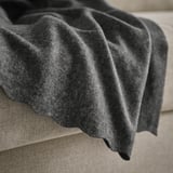 Una suave manta de vellón gris oscuro sobre un sofá o cama beige. La textura se ve acogedora y acogedora, ideal para brindar calidez.