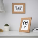 Marcos de madera: mariposa, corazón. Uno en la estantería con cactus, libros; uno cuelga.