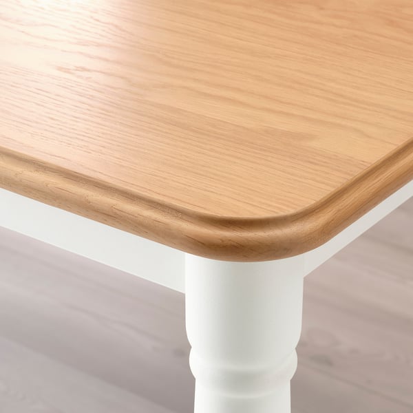 Primer plano de una mesa de comedor robusta y elegante con tapa de madera lisa y duradera y fuertes patas blancas.