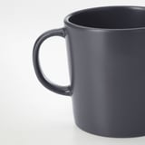 Taza gris oscuro, mate, con asa robusta, que descansa sobre una superficie lisa.