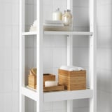 Estantes blancos de baño con toallas cuidadosamente apiladas y cajas de bambú, una de las cuales contiene algodón.