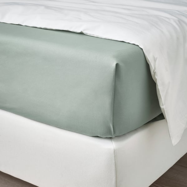 Cama cuidadosamente hecha con sábana de algodón verde grisáceo y almohadas blancas.