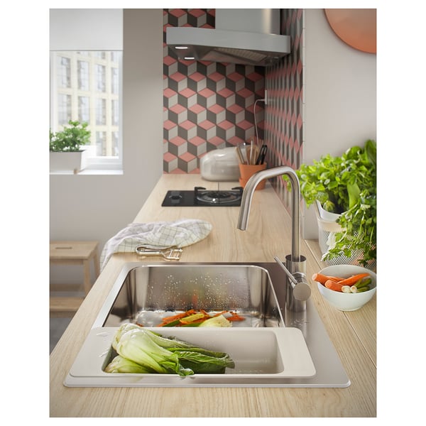 Cocina moderna con encimera de madera clara, placa para salpicaduras de azulejos geométricos, fregadero de acero inoxidable, verduras y plantas.