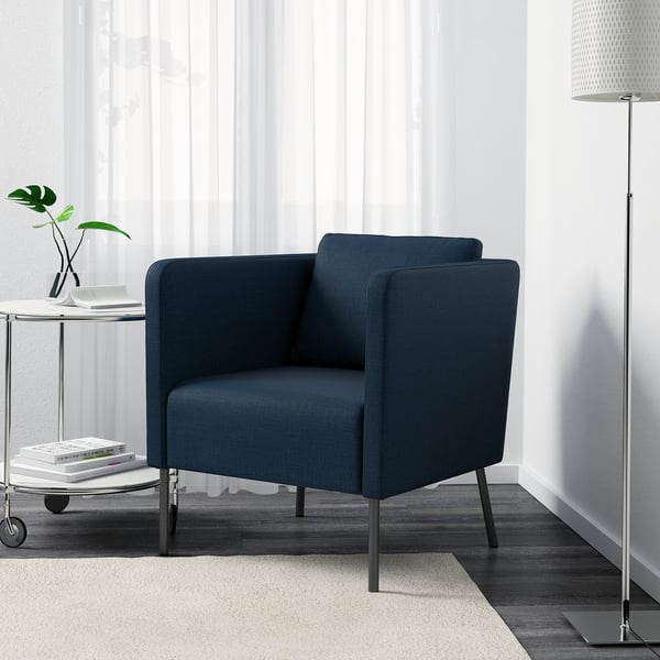 Sillón azul con cojín de respaldo ajustable, reposapiés y lámpara de pie alta a su lado.