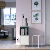 Mueble de almacenaje minimalista, blanco, patas de madera, libros, planta, taburete, debajo de la ventana.