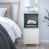 Mesita de noche EKET blanca y verde junto a la cama con libros y armario.