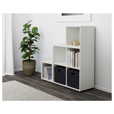 Estantería modular blanca EKET, con cajas abiertas y de almacenamiento. Tiene capacidad para libros y contenedores suministrados. Fijado a la pared para mayor estabilidad.