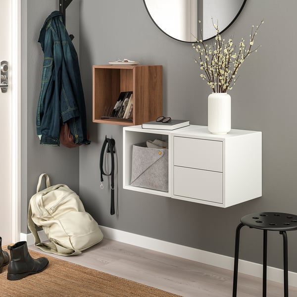 Entrada moderna con armarios EKET en blanco y madera, que sostienen libros, jarrones y accesorios.