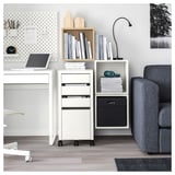 Moderna configuración de oficina con unidad de almacenamiento EKET blanca, sofá gris, computadora portátil, decoraciones de madera y libros.