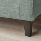 Primer plano de un elegante sofá tapizado en esquina con pata de madera oscura sobre suelo de madera.